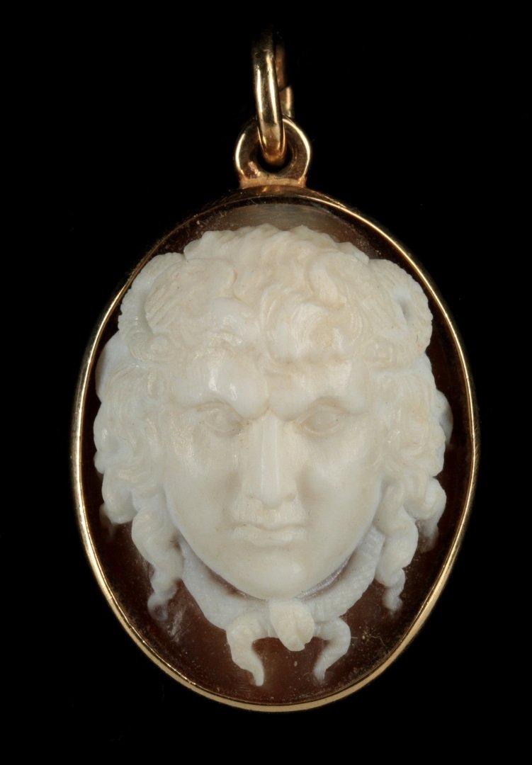A ZEUS AMMON CARVED SHELL CAMEO PENDANT: A vintage oval carved shell visage of Zeus Ammon displayed in an unmarked 14k gold bezel, measures 1 inch without the bail. 7.5 grams.
