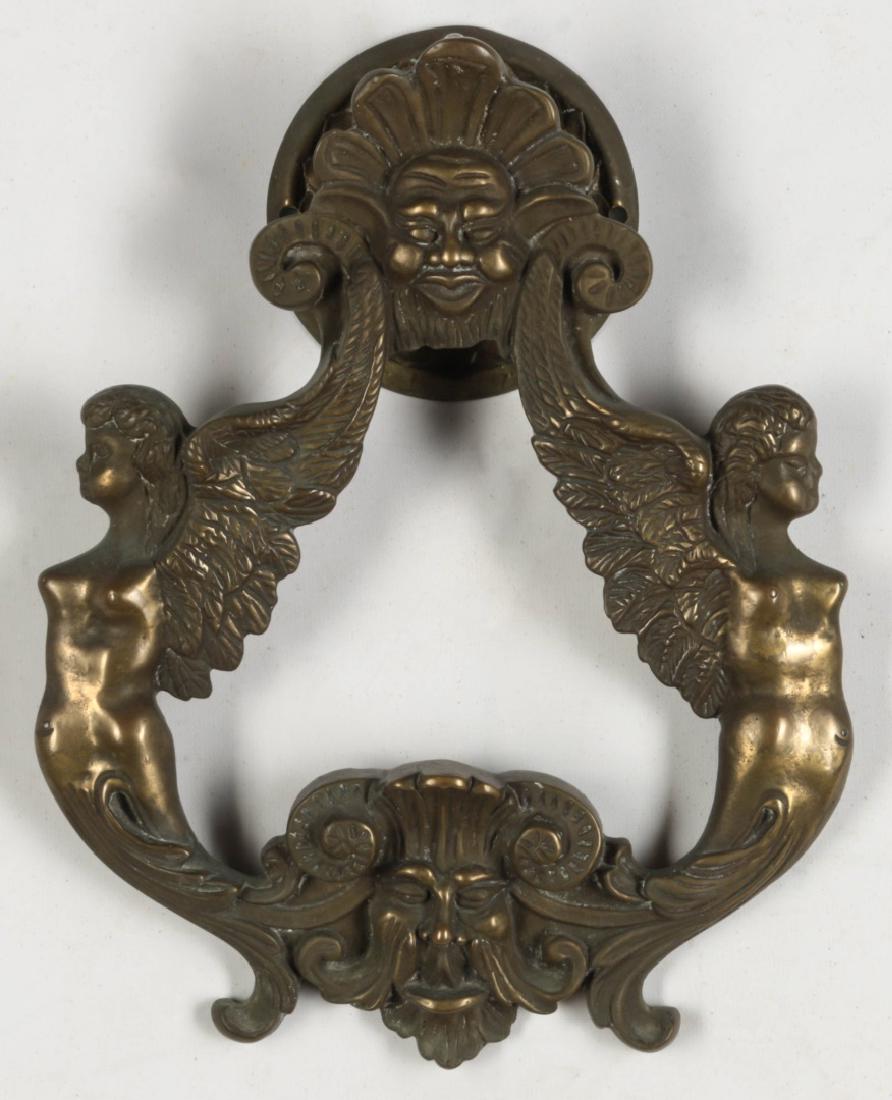 A MASSIVE BRASS DOOR KNOCKER WITH WINGED FIGURES: A massive door of circular form with opposing winged figures and horned male mask. Measures 11.75 x 9 inches, with hardware.