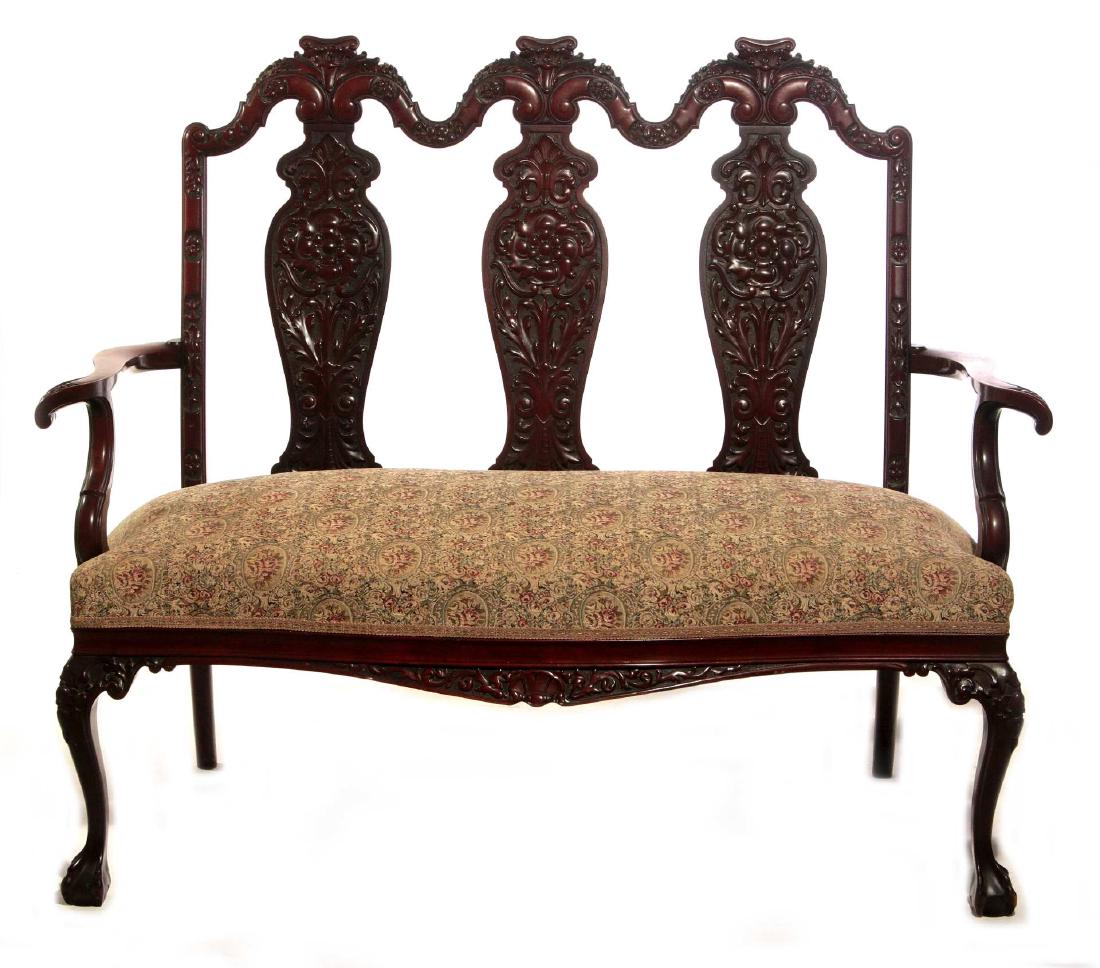 A HIGHLY CARVED CHIPPENDALE LEG MAHOGANY BENCH: A nice quality circa 1900 hall bench, the arched and carved crests each centering an Ionic capital and overflowing carved foliate above vasi-form backs with carved rosettes and foliate on a stapled gr