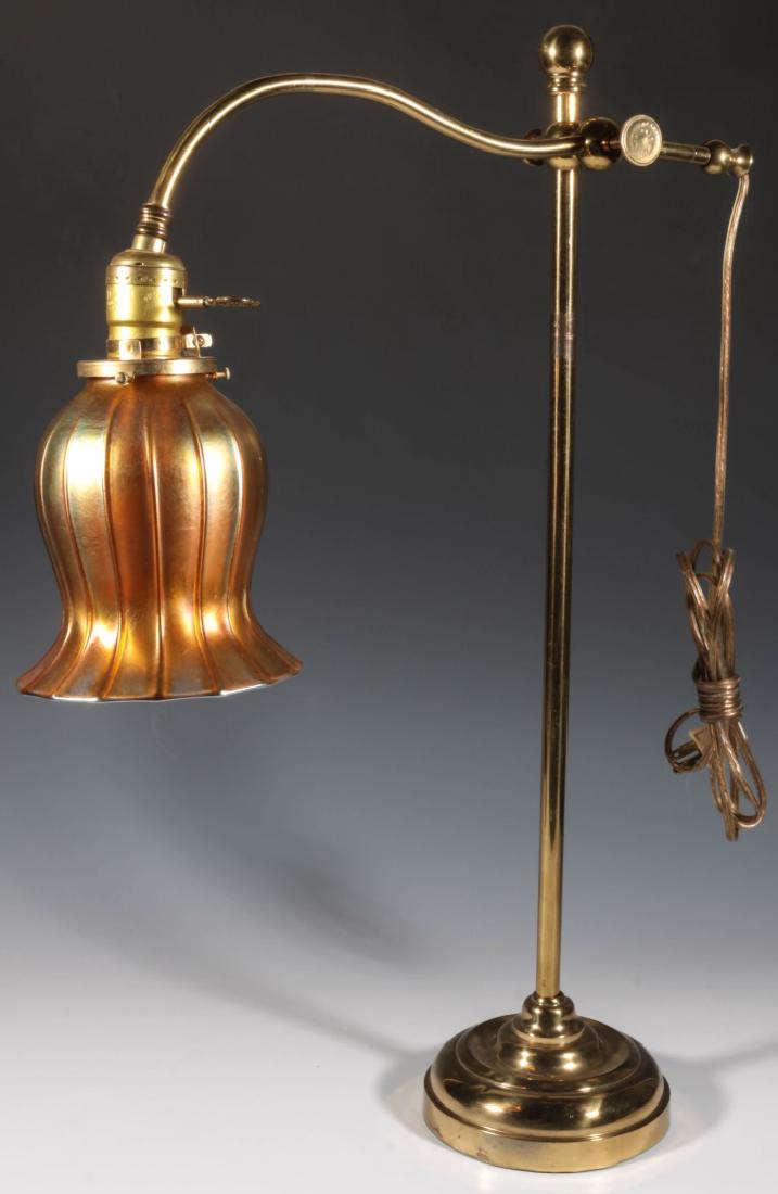 A BRASS TABLE LAMP DATED 1874 WITH QUEZAL SHADE: An adjustable bridge lamp with coined edge adjustment knob stamped with lettering 'H.C. Beck Ptd Mar. 10 74', and fitted with a gold iridescent shade signed Qeuzal. Lamp measures 23.5 x 15 inches. Sha