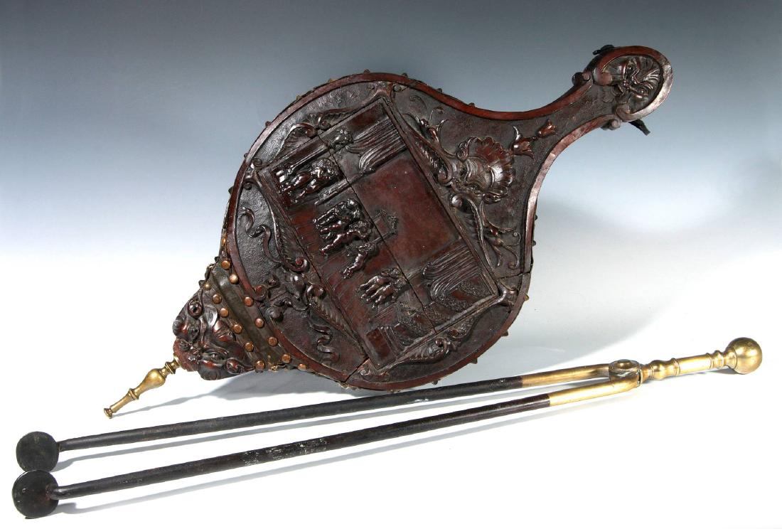 HIGHLY CARVED 19THCENTURY WALNUT FIREPLACE BELLOWS: With a scene of cupids in an interior, plus a pair of fireplace tongs. Bellows measure 28 x 13.25 inches, tongs 30 inches.