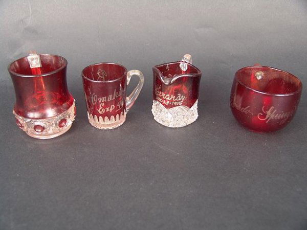 FOUR PCS OF ANTIQUE RUBY FLASH GLASSWARE: Omaha Expo 2.25 inches high, El Dorado Springs mug is 2.5 x 3.25 inches, Gracie 1905 pitcher is 2.25 x 3.5 inches plus another measuring 3 x 3 inches. All show typical signs of loss to ruby.