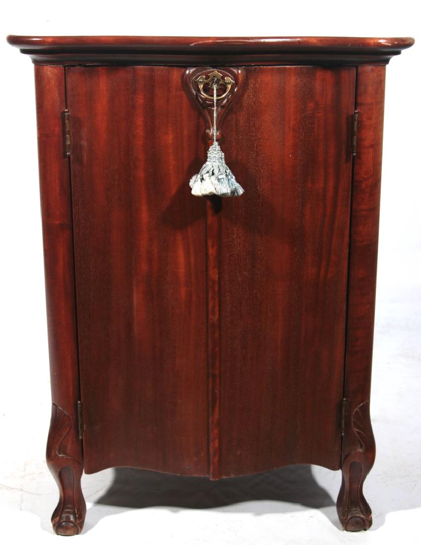 CIRCA 1900 MAHOGANY MUSIC BOX DISC STORAGE CABINET: A scarce ribbon mahogany serpentine form cabinet designed for compatibility with the Regina serpentine music boxes no. 50 and no. 155 (Reginaphone), both of which are also represented in this auction,