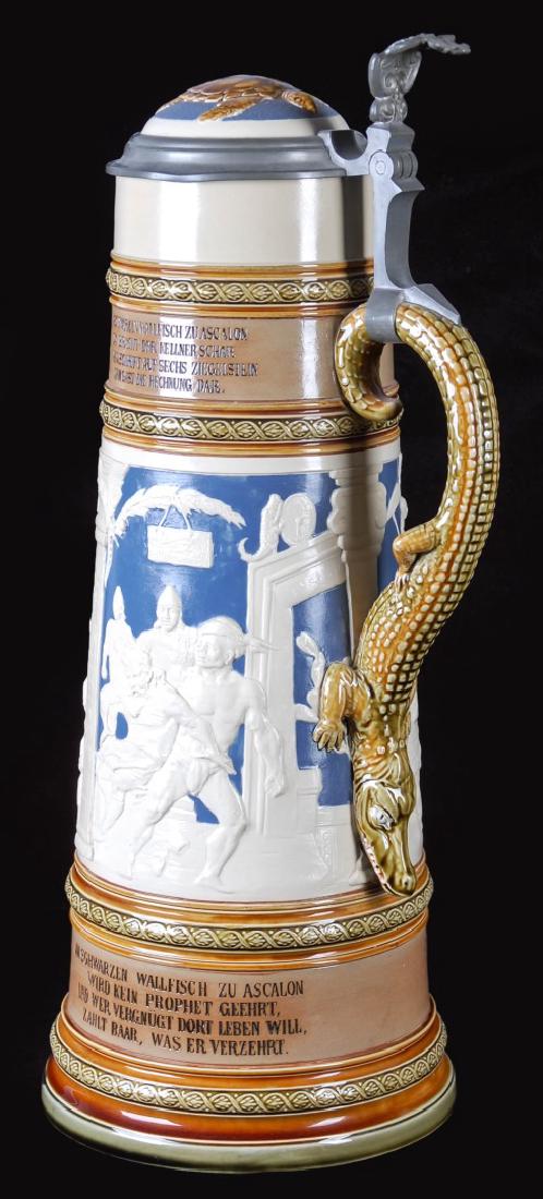 A THREE LITER METTLACH STEIN BLACK WHALE OF ASCALON: A commemoration of an old German story and drinking song, the tale told in white relief scenes against a blue ground, bands of glazed decoration and incised lettering, a large alligator figural handle