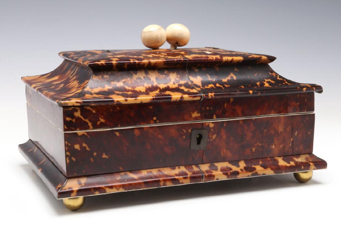 A 19TH CENTURY TORTOISE VENEER SEWING BOX: Of sarcophagus form, the tapered rectangular case with hinged lid centering a conforming tablet on cavetto sides surmounted by twin bone spherical finials, opening to a fitted yellow silk interior of 