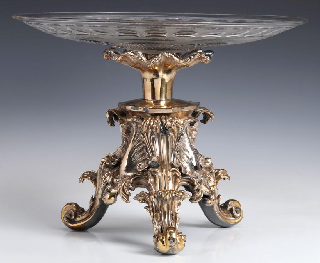 A SILVERED BRONZE AND CUT CRYSTAL ROCOCO TAZZA: The base modeled of overlapping acanthus leaves rising from four scrolling feet adorned with flower heads cast separately and pinned to the base supporting a cut crystal shallow basin of striated lobe