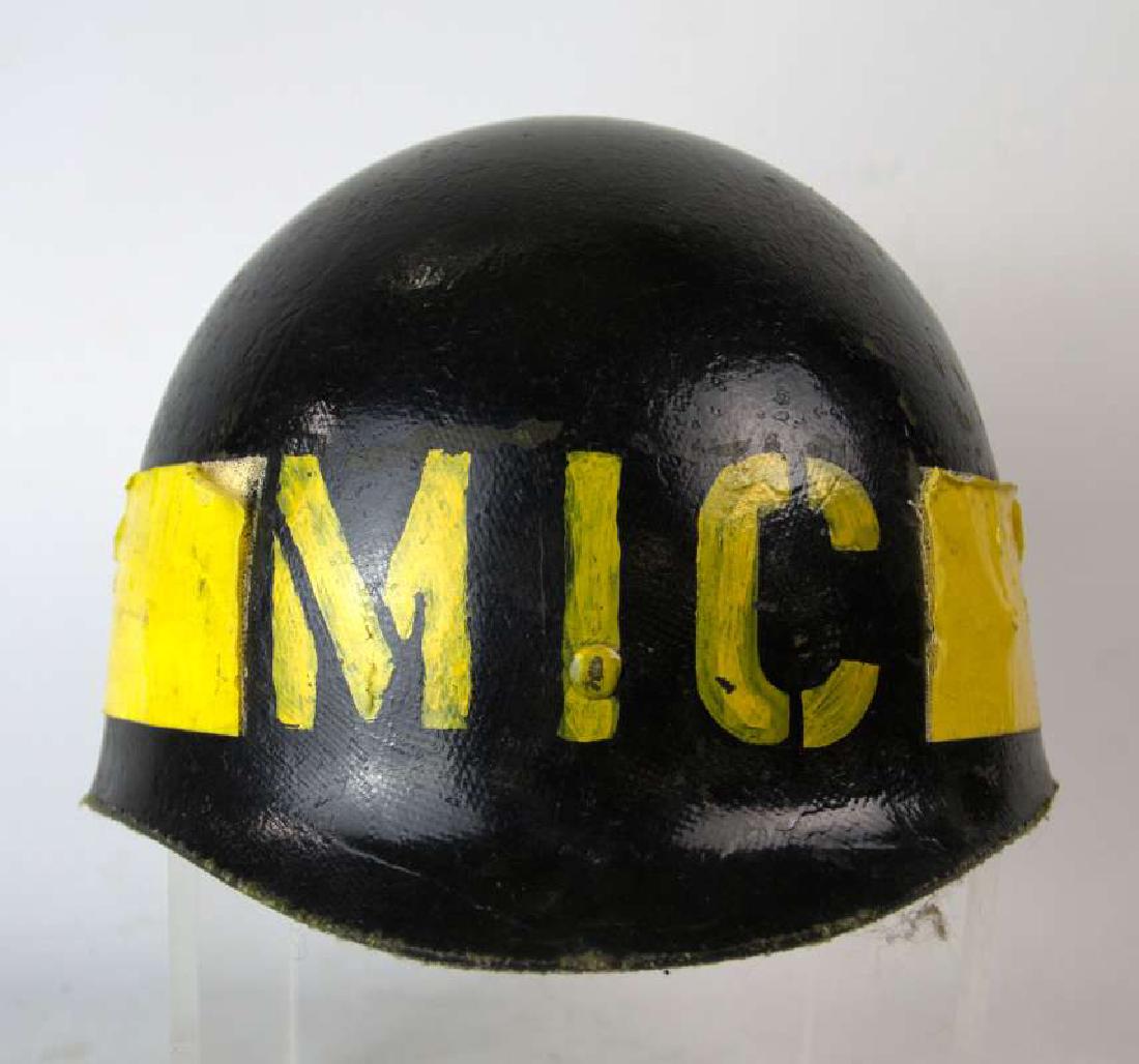 US ARMY GROUND FORCES MIC HELMET LINER: Interesting M-1 helmet liner painted black and with stenciled MIC on the front, Army Ground Forces roundel painted to the left side, and yellow tape applied between. Leather sweatband with canvas stra