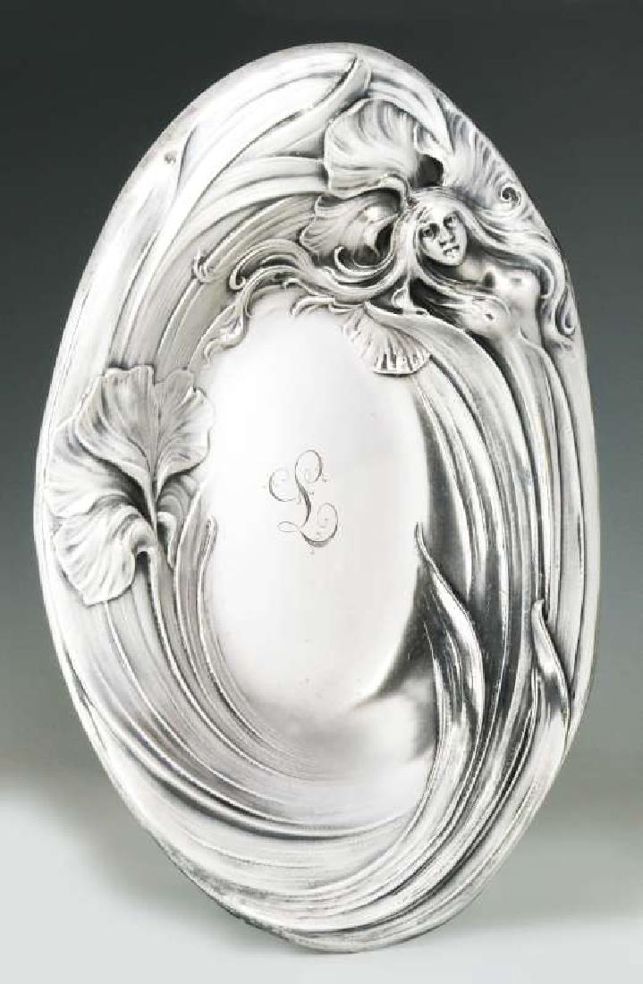 AN ART NOUVEAU STERLING SILVER TRAY WITH MAIDEN: The wide rolled edge design of flowing leaves and blossoms incorporating a semi-nude maiden in relief, a central monogram, stamped unicorn maker's mark of Mauser Manufacturing Co. on the under side al