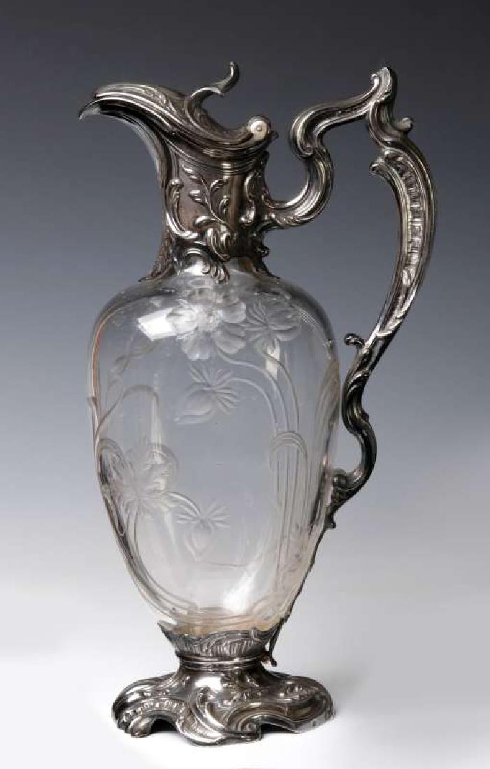 A FINE BACCARAT CRYSTAL CLARET JUG IN METAL MOUNTS: Rococo influence silver plated mounts, the crystal body decorated with intaglio carved flowing tendrils and blossoms, signed Baccarat in the metalwork underside of the foot. Measures 12.25 x 7 inches.
