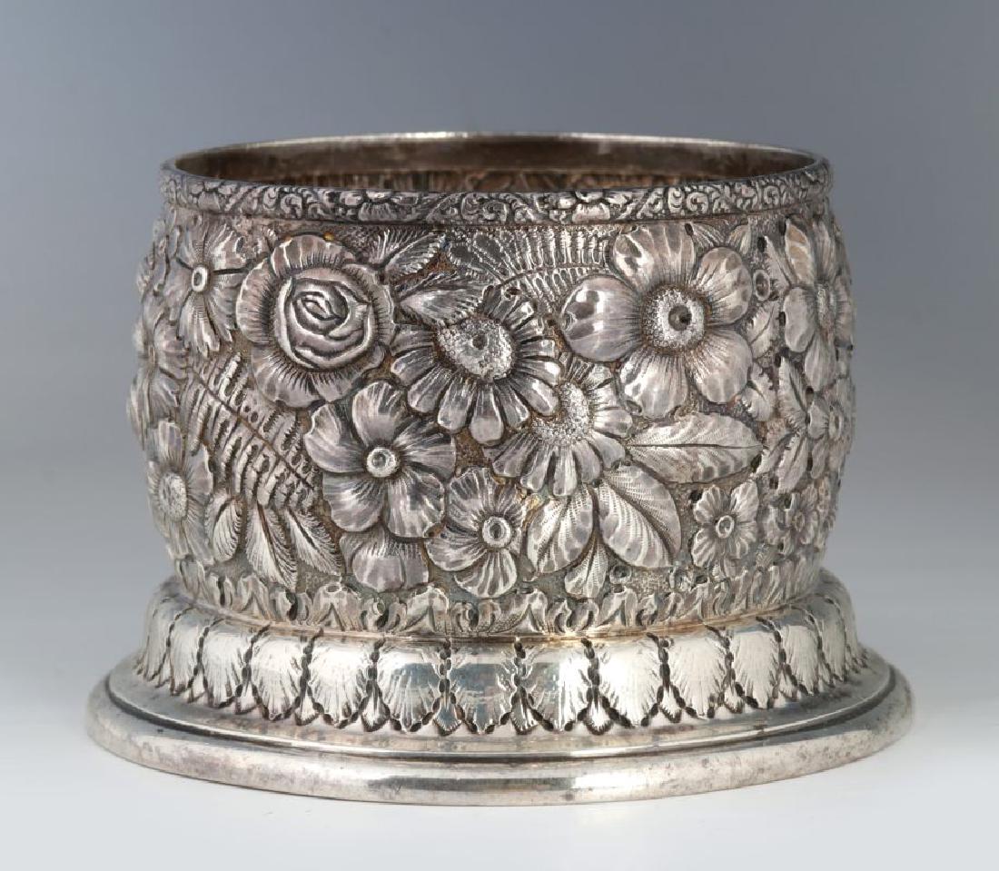 UDALL & BALLOU STERLING SILVER WINE BOTTLE COASTER: Repousse florals, stamped maker's marks underside of the base 8094M 8785, sterling silver. Weight 5.85 troy ounces. Measures 3 x 4 inches. We happily provide seamless in-house packing and shipping ser