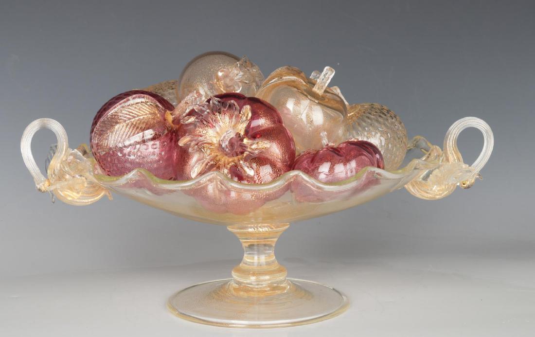 AN ITALIAN VENETIAN GLASS CENTERPIECE WITH FRUIT: The aventurine bowl with circular foot, knopped stem supporting a shallow bowl with scalloped edge and flanked by applied swan-form handles, filled with blown and appliqued pink and aventurine glass p