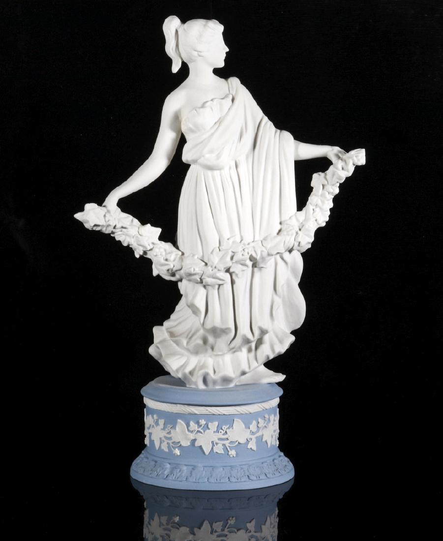 A WEDGWOOD JASPER FIGURE OF CLASSICAL MAIDEN: Figure of a classical maiden in robe with garland atop circular plinth sprigged with white ivy on blue, marked Wedgwood Made In England. Measures 10.25 x 6.25 x 3.75 inches. We happily provide seamles