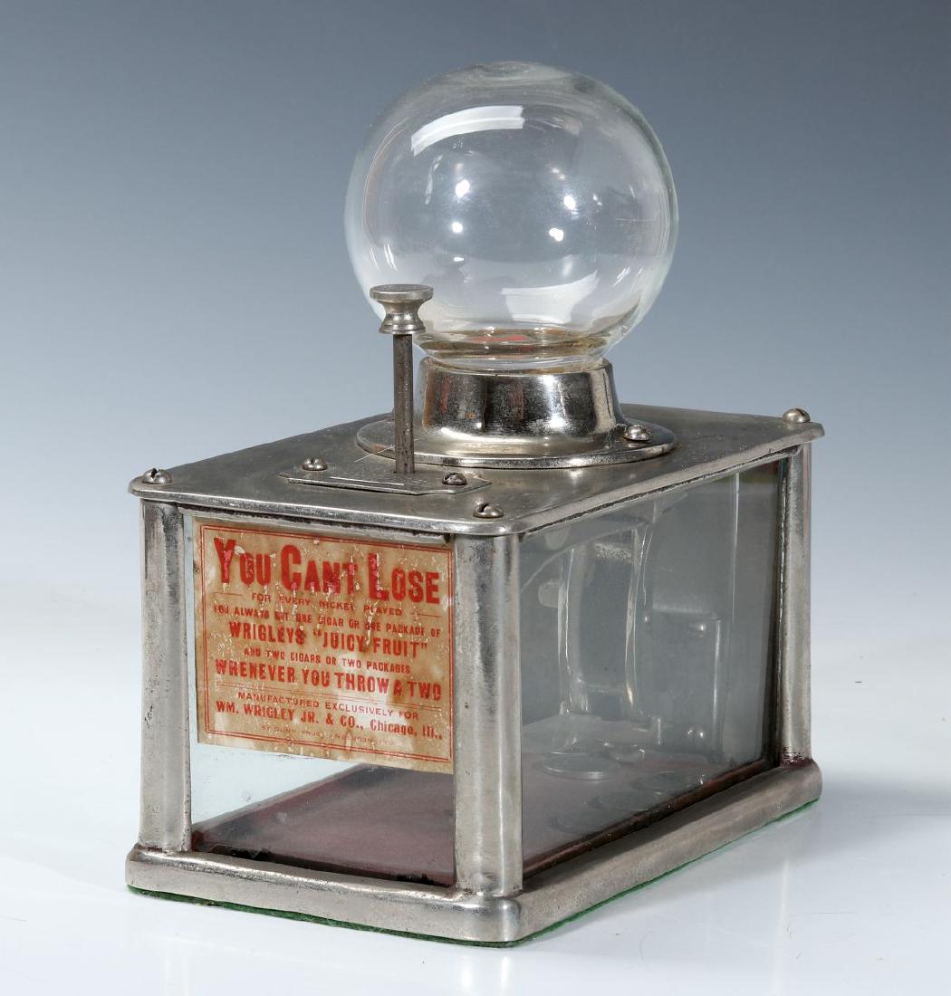 A 1906 'CAN'T LOSE' WRIGLEY GUM NICKEL DICE GAME: A rare dice game trade stimulator, the nickel plated housing with glass orb over money box with glass on three sides, front decal, top plate with plunger, inside the glass orb the dice are 'thrown.' M
