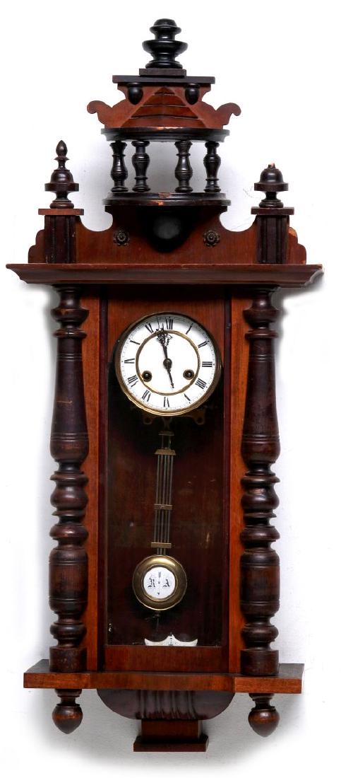 A PHILLIP HAAS AND SONS RA REGULATOR: The wall hanging clock with turned wood half-columns and finials topped by a fancy cupola, carved bracket, porcelain enamel Roman numeral dial and RA pendulum, time and strike. Measures 38.5 x 16.5 x