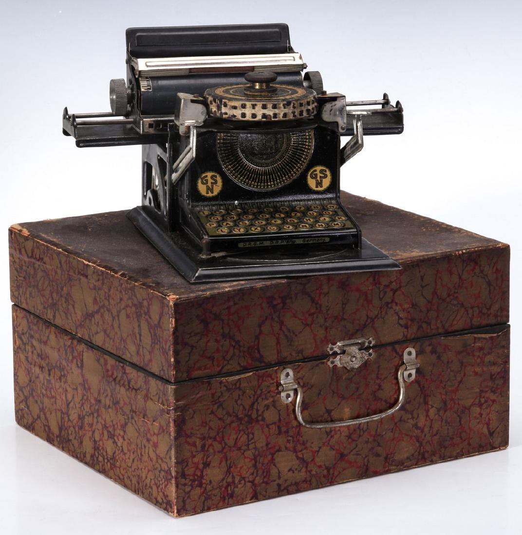 A GERMAN GSN METAL LITHO TYPEWRITER: Variation 2 - GSN metal litho with box. Text on typewriter: GSN, DRGM DRP ANG, Germany. Typewriter measures approx.4 inches wide by 7 inches long by 4.5 inches tall. Box is approx.8 inches wide by 8 i