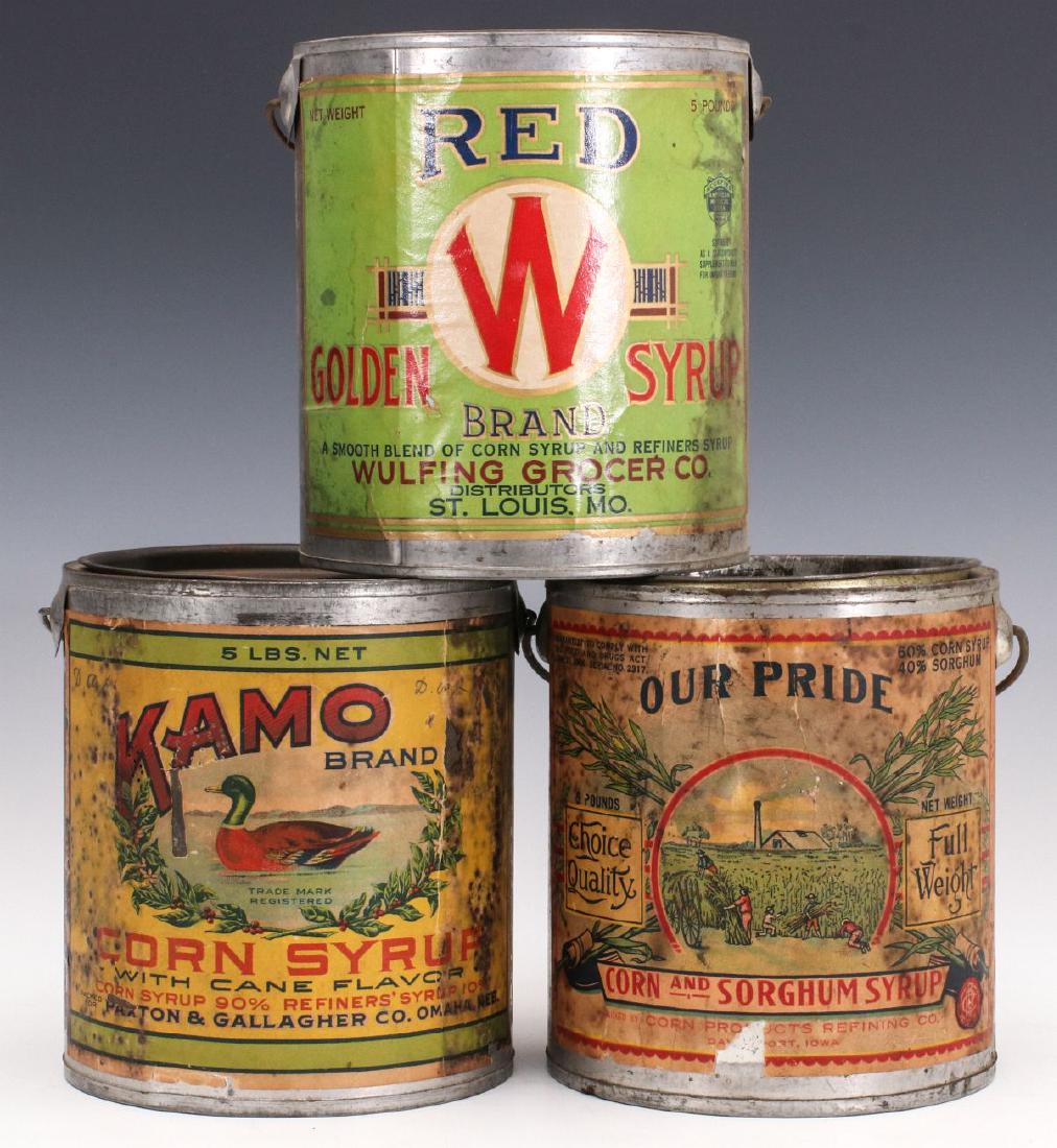 THREE TIN SYRUP PAILS WITH COLORFUL PAPER LABELS: Red W Golden Syrup, Kamo brand corn syrup, Our Pride corn and sorghum syrup in tin pails with litho paper labels. Measure 6 x 5 inches each. We happily provide seamless in-house packing and shipping s