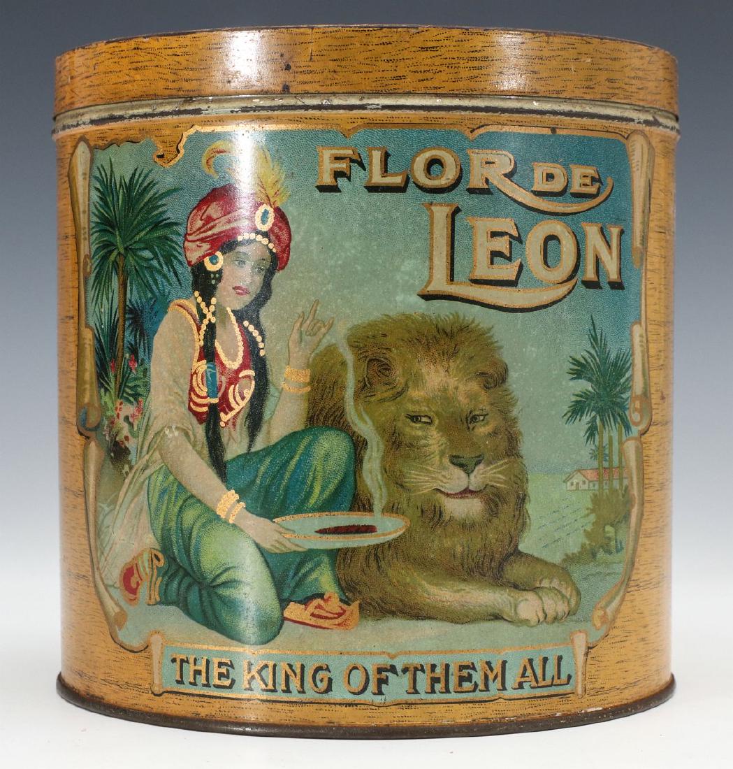A TIN LITHOGRAPH CONTAINER FOR FLOR DE LEON CIGARS: The covered canister lithographed with striking graphics of a maiden serving up a cigar to an African lion on two sides and the cover, 'THE KING OF THEM ALL', faux wood grain background. Measures 5.25