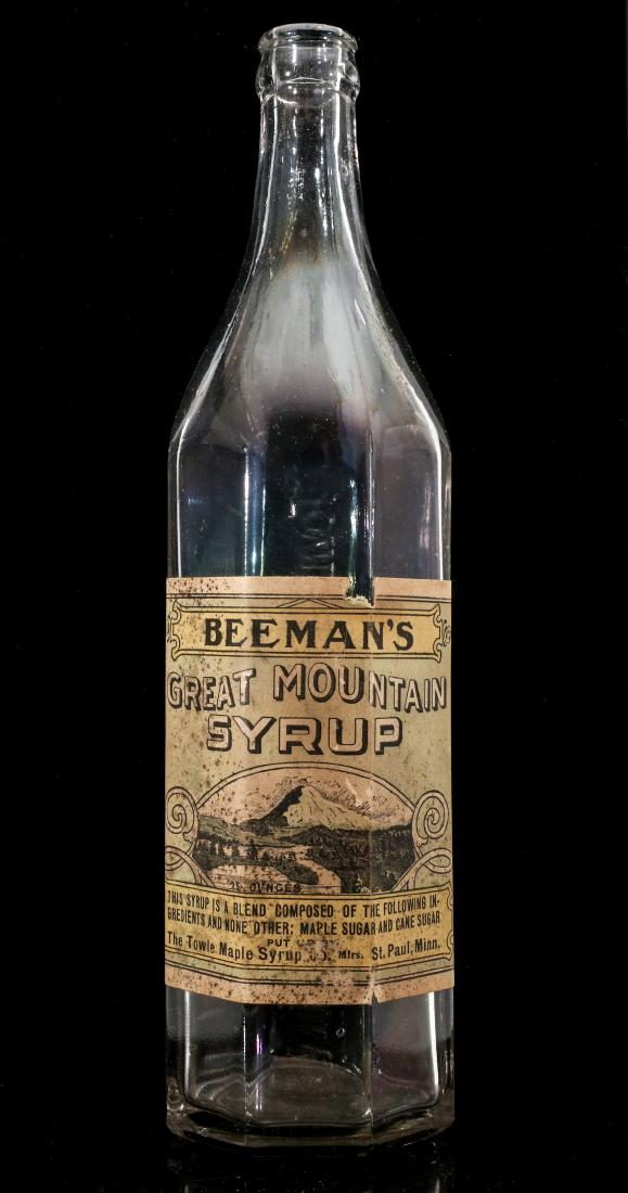 A BEEMAN'S / TOWLE MAPLE SYRUP BOTTLE WITH LABEL: The product bottle for BEEMAN'S GREAT MOUNTAIN SYRUP, 'Put Up By the Towle Maple Syrup Co.' The back side is embossed TOWLE MAPLE SYRUP COMPANY. measures 11.5 inches. We happily provide seamless in-ho