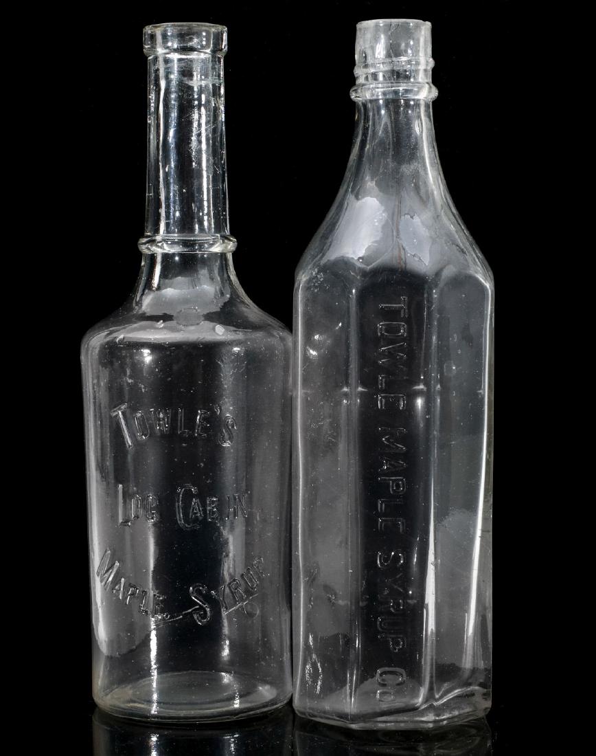 TWO EARLY AND UNUSUAL TOWLE'S MAPLE SYRUP BOTTLES: One unusual example being the circular example embossed TOWLE'S LOG CABIN MAPLE SYRUP. Plus an unusual example with eight flat sides interrupted by a smooth semi-circle portion rounded to better displ