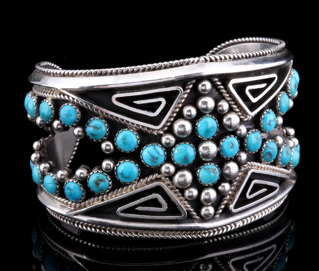 A BILLY BETONEY CUT-OUT STERLING CUFF W/ TURQUOISE: The uniquely designed cuff with cut-out openings on either side, the well-balanced design of four sterling silver path of life channels composed with lines of calibrated blue turquoise stones set in s