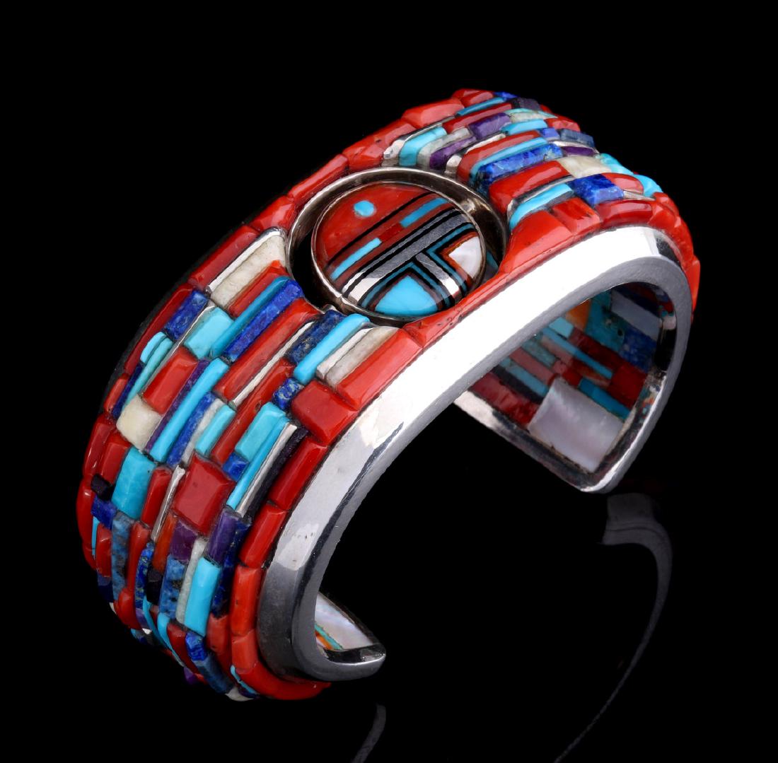 A FINE GILFORD TSATTIE (1965-2013) CORN INLAY CUFF: A very well crafted and unusual Zuni inlay cuff bracelet by Gilford Tsattie (1965-2013) of Zuni New Mexico, the double sun face spinner centered on a wide cuff with raised corn-style inlay of coral, t