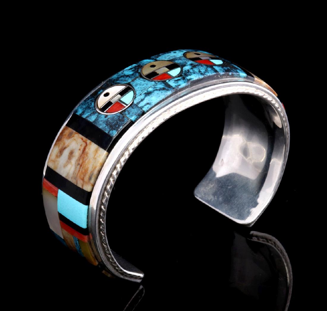 AN INLAID SUNFACE BRACELET SIGNED GMC FOR CALAVAZA: The Zuni inlaid cuff by Gilbert & Mildred Calavaza, intricate inlay of turquoise, jasper, coral, mother of pearl, jet with three traditional sunface designs, the inlay is set in a fabricated sterling