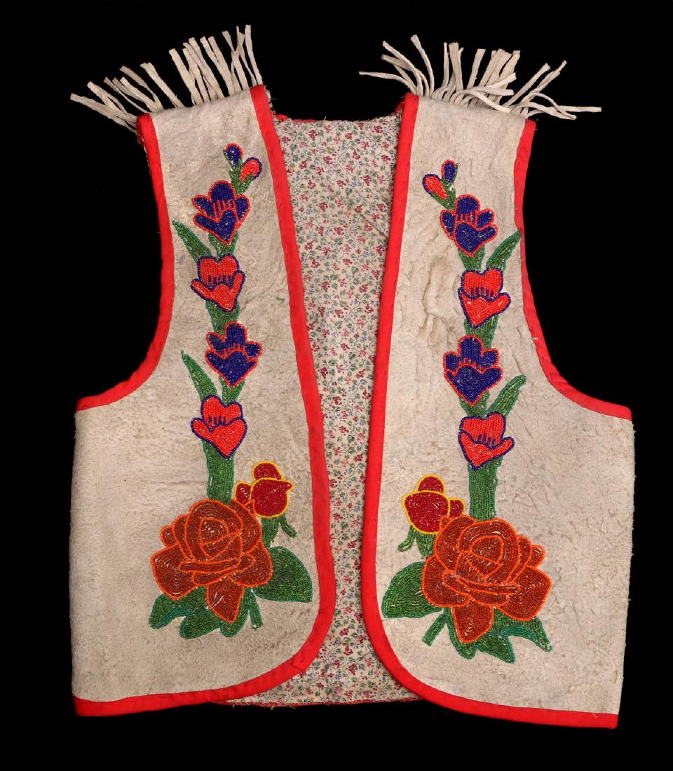 A LATE 20TH C. CHIPPEWA INDIAN BEADED CHILD'S VEST: The tanned hide vest lined with trade cloth and trimmed in red, beaded floral decoration. 13 inches shoulder to shoulder, 19 inches in length, 18.5 inches. We happily provide seamless in-house packing