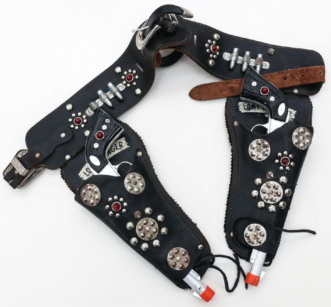 A LONE RANGER DOUBLE HOLSTER BELT AND CAP GUNS: A child size genuine black leather belt with double holsters, Lone Ranger logos to each holster, metal bosses with red plastic jewels, five dummy silver bullets, silver toned single claw buckle; also
