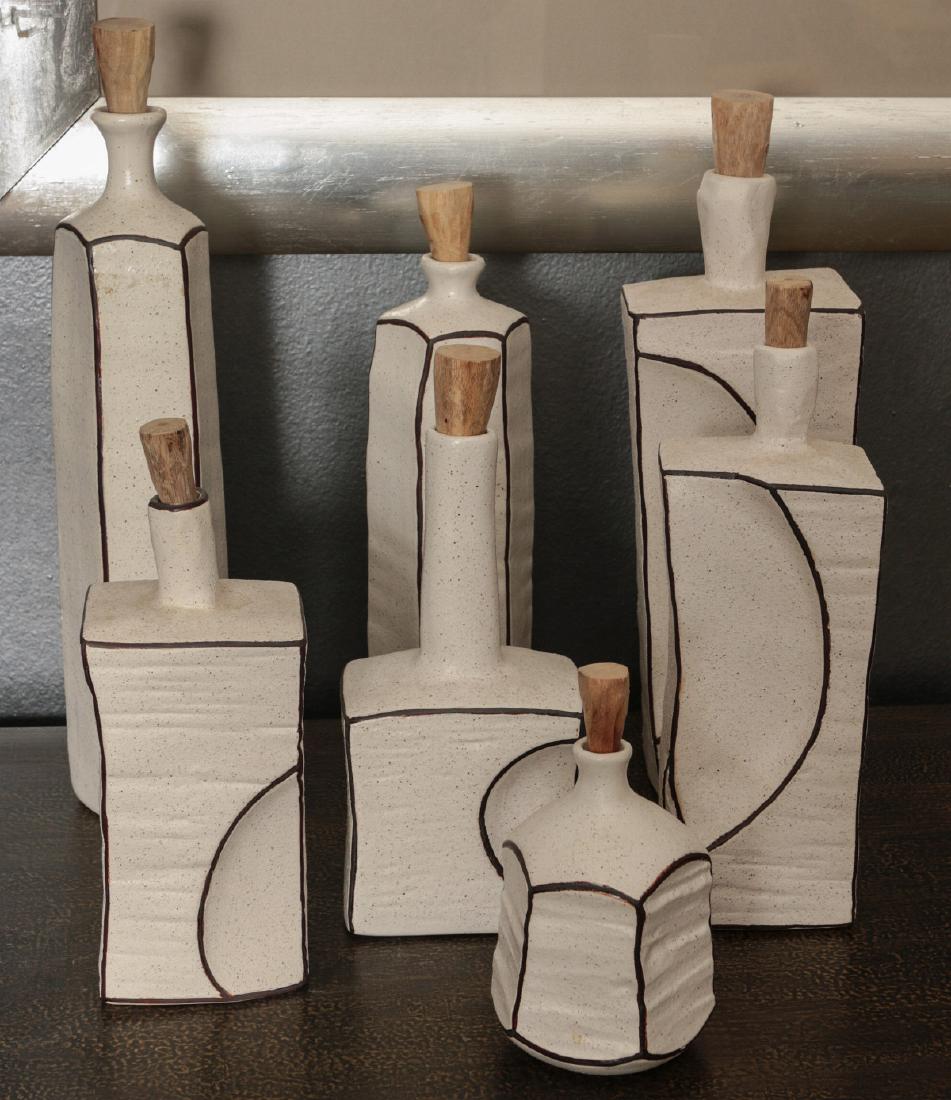A COLLECTION CONTEMPORARY STUDIO POTTERY BOTTLES: Seven different cut and sculpted stoneware bottles, buff colored glaze with brown speckles and brown trim. Sizes range from 6.5 x 3.5 up to 16.25 x 3 inches. We happily provide seamless in-house packi