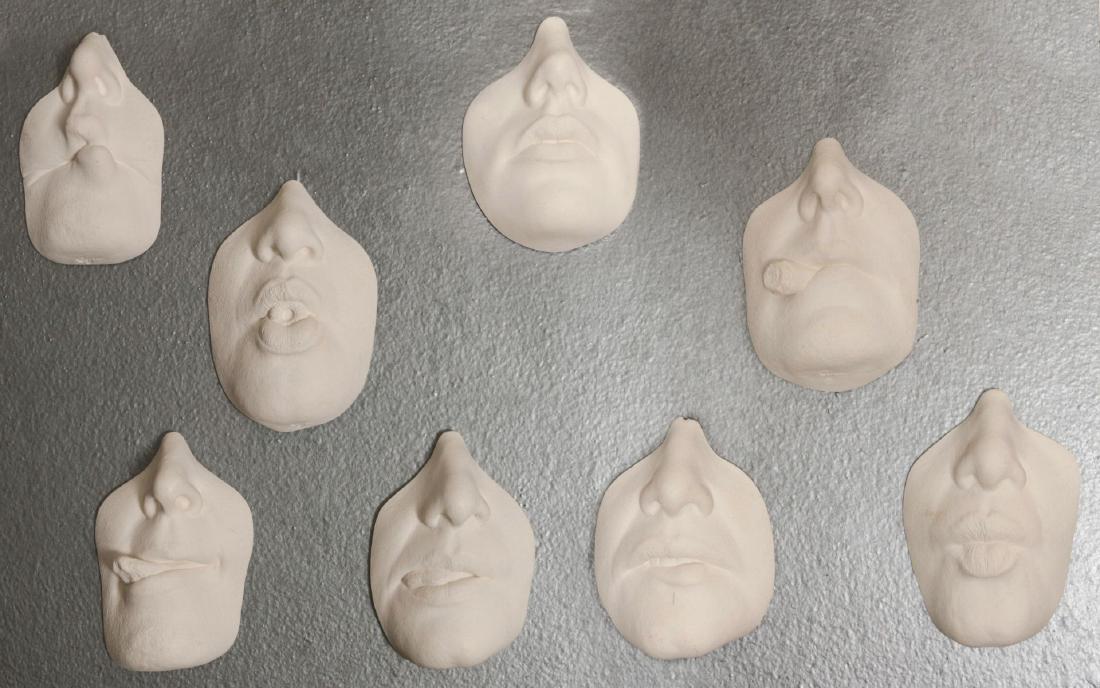 A GROUPING OF ARTIST SIGNED WALL HANGING MASKS: Eight sculptures depicting various facial expressions, various positions of the lips including with a Lifesaver, Cigar, etc. Each measures approximately 4.5 x 3 inches. We happily provide seamless in-