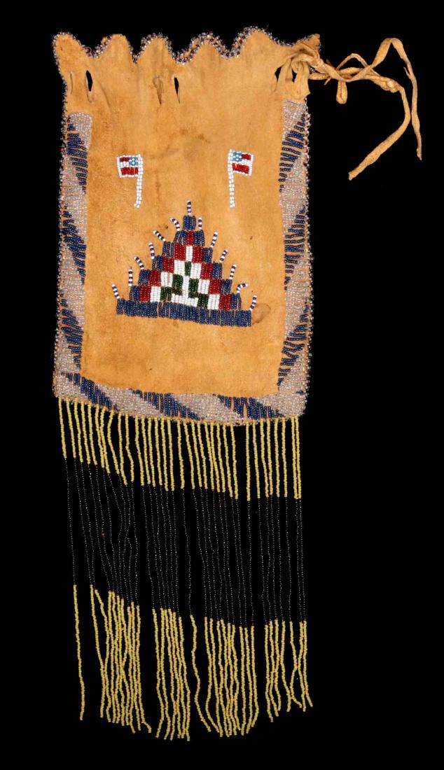 A FORT SILL APACHE BEADED HIDE BACK: The native tanned hide bag with draw string top, beaded trim along the scalloped top, lazy stitch beading down each side and across the bottom of each side, one side is decorated with American flags a