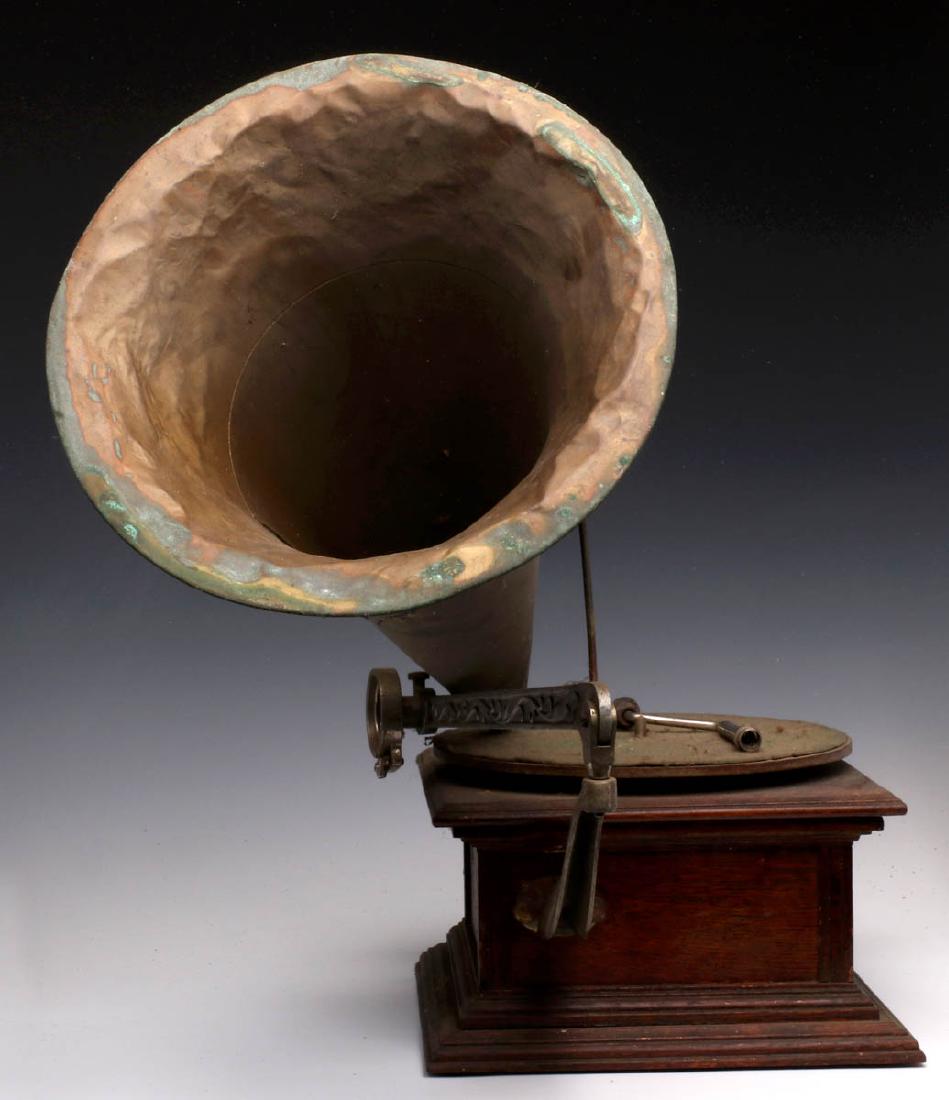 AN EARLY FRONT MOUNT BRASS HORN PHONOGRAPH: The oak case machine with simple flat corner columns, nickel plated iron support arm and ornate aluminum tone arm, solid brass horn, a reproducer on the tone arm. Measures 22 x 24 inches. We happily p