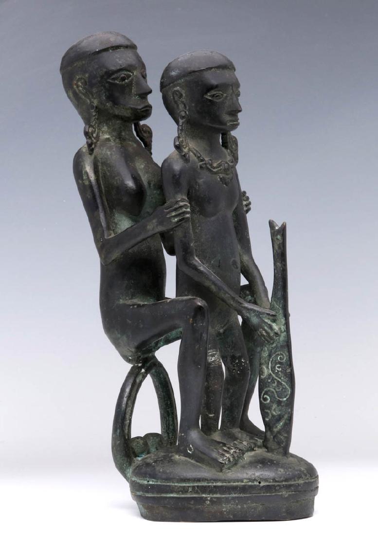 AN AFRICAN BRONZE FIGURE GROUP: A seated female figure poses with a smaller standing figure holding a stylized weapon. Measures 11.25 inches. We happily provide seamless in-house packing and shipping services on nearly everything we