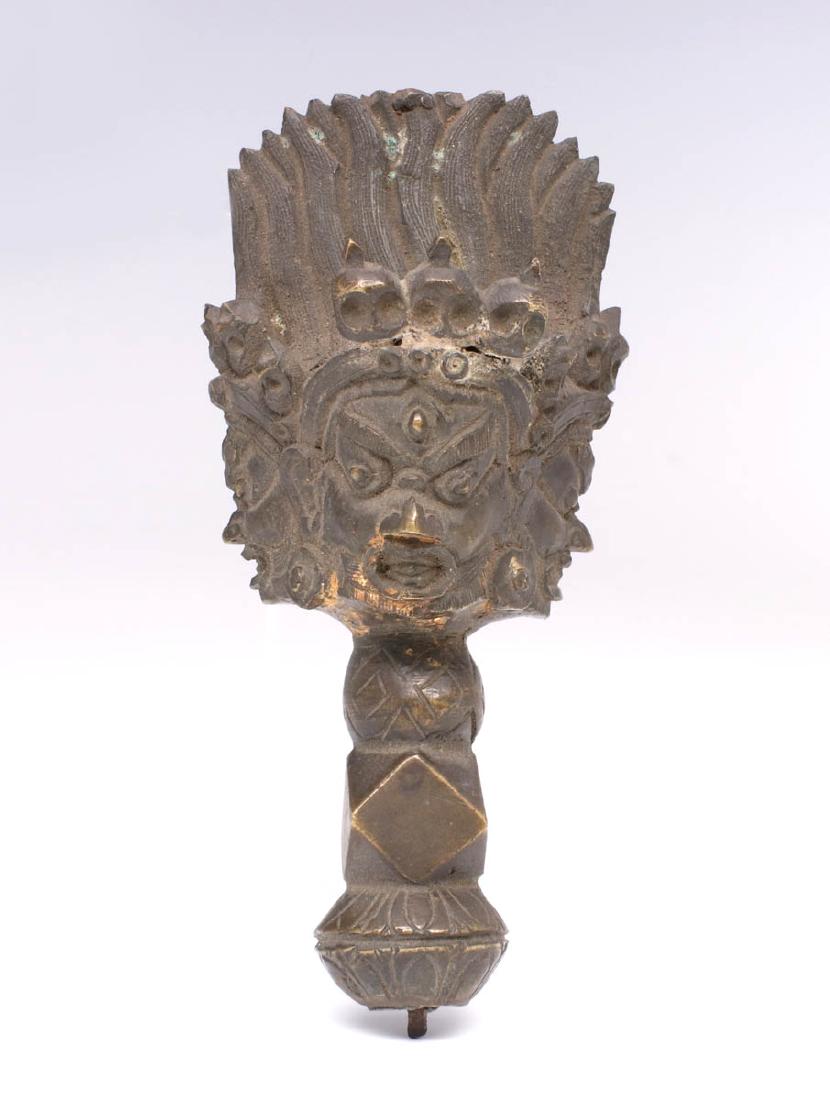 A TIBETAN BUDDHIST BRONZE CASTING/DAGGER HANDLE: The cast bronze handle or other portion of a larger object, a crown with multiple masks, each with the five skulls associated with Mahakala. Measures 5 inches. We happily provide seamless in-house pac