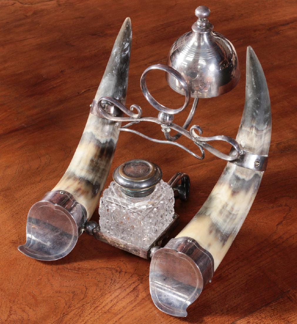 ANTIQUE SILVER-MOUNTED HORN INKWELL WITH BELL: The parallel horns with silver-plated mounts and central cut glass inkwell, the upswept horns with scrolling carriage connecting the two and supporting a silver tap call bell, a central finger loop an
