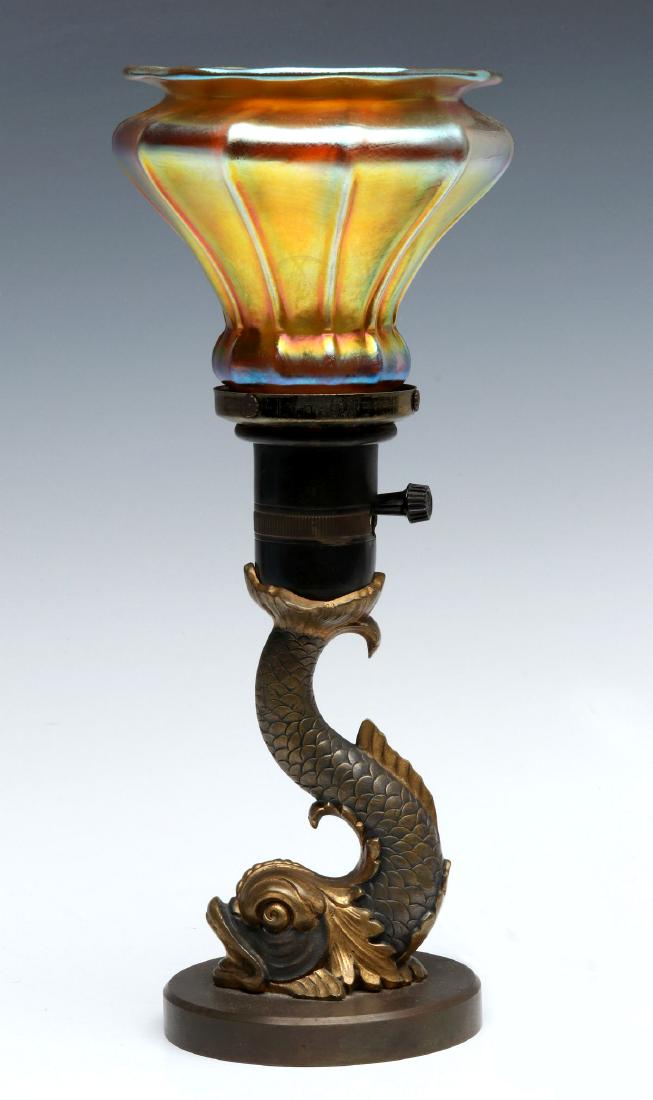 AN EARLY 20TH CENT BRONZE LAMP WITH STEUBEN SHADE: The parcel gilt and patinated bronze dolphin figural table lamp fitted with a gold aurene shade signed Steuben. Measures 12 x 4.75 inches overall, 2.25 inch fitter. on the shade. We happily provide se