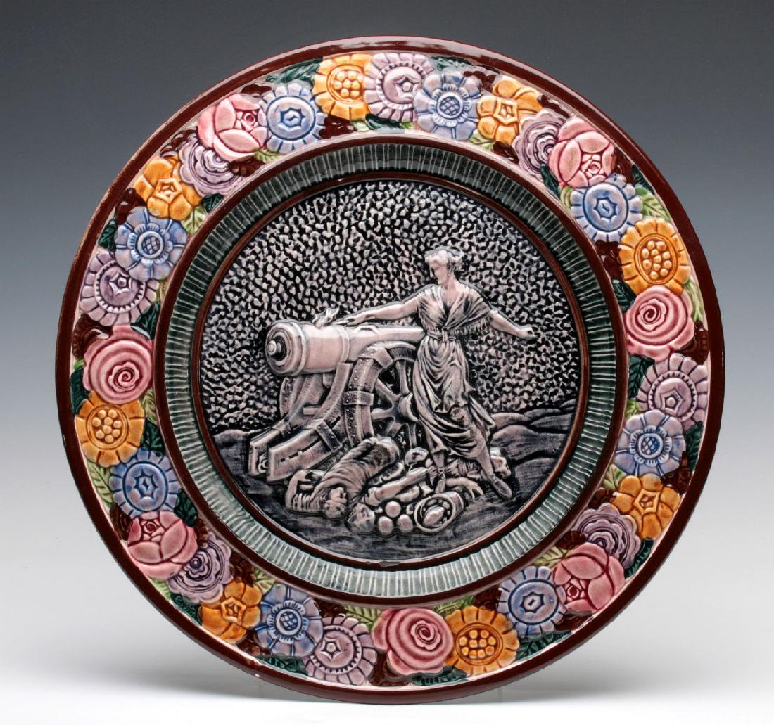 A LARGE CONTINENTAL POTTERY MAJOLICA PLAQUE: The border of raised stylized flower heads centered by an image of Margaret Corbin at Fort Washington. Measures 1.5 x 16.75 inches. We happily provide seamless in-house packing and shipping services o