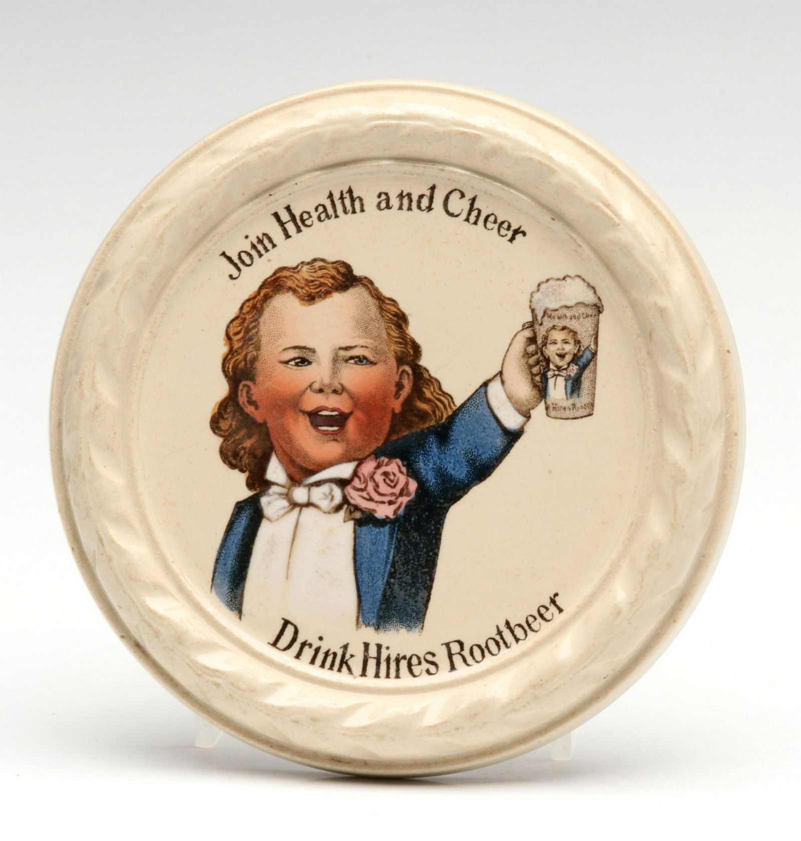 A VERY RARE METTLACH POTTERY HIRES ROOT BEER COASTER: The circular pottery coaster or tray with dish edge, the Hires boy with mug raised and slogan 'Join Health and Cheer' with 'Drink Hires Root Beer.' Signed Villeroy and Boch, Mettlach in green back sid