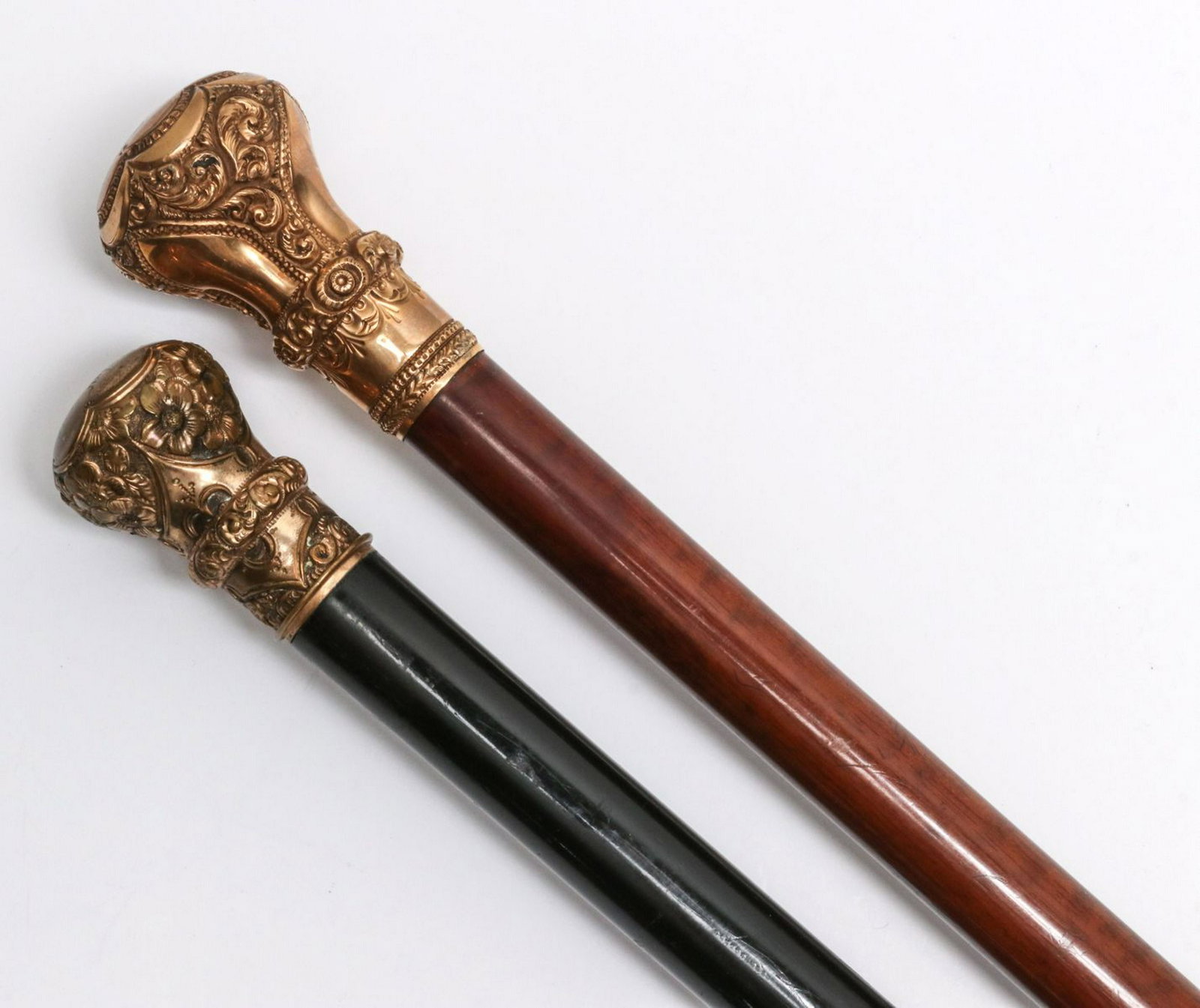TWO WALKING STICKS WITH ORNATE CHASED GOLD FILL HANDLES: Two Victorian walking sticks, one ebonized and one of finished wood, each with super ornate chased and engraved knob handle with scrolls in high relief hand crafted repousse. Measures from 35 to 25.5 