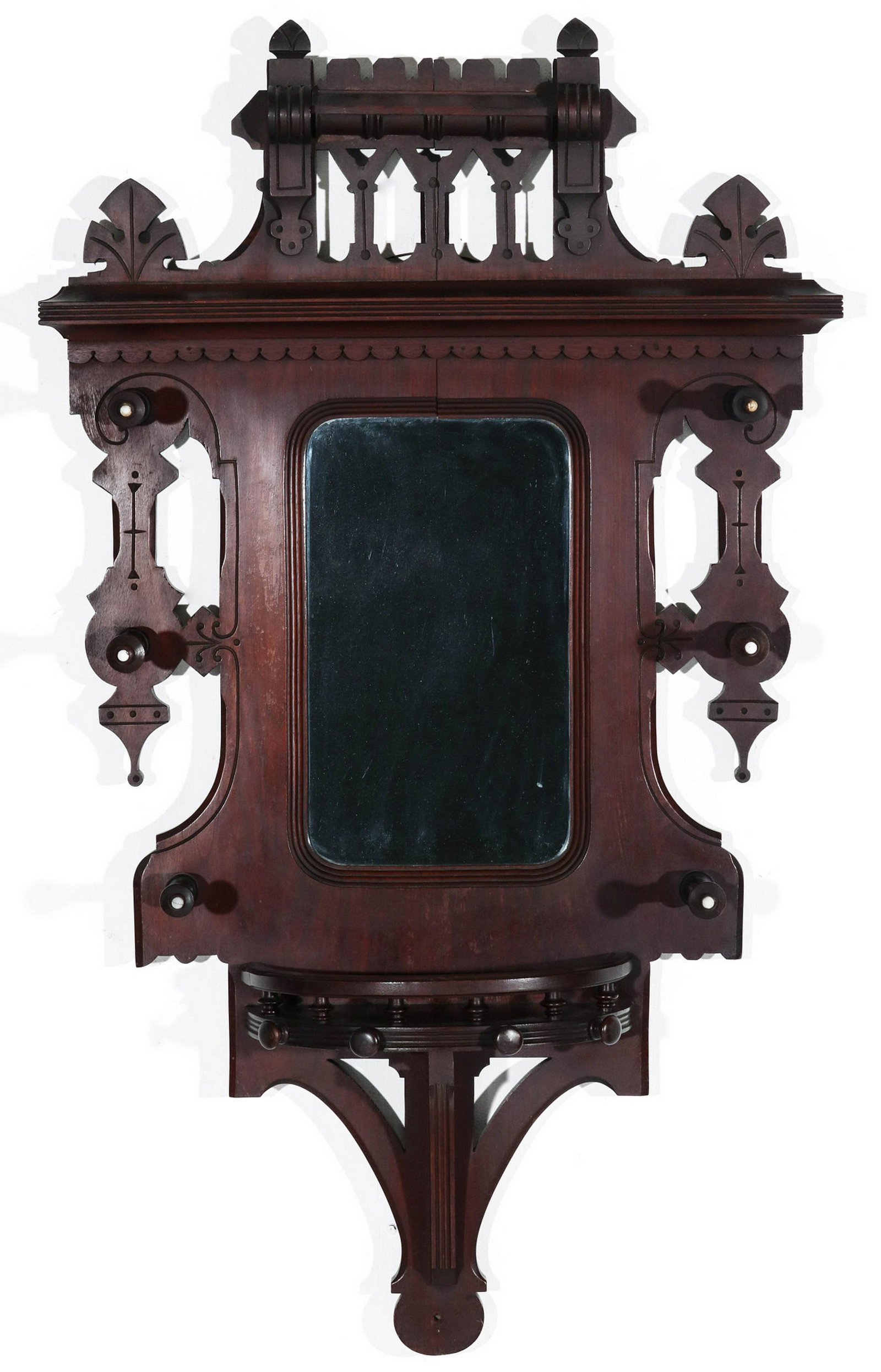 A VICTORIAN WALNUT EASTLAKE STYLE MIRRORED HAT RACK: The elaborate crown with palmettes and ornate openwork over a central mirror flanked by coat or hat pegs tipped in porcelain, the demilune shelf with gallery above the lower bracket shelf support. Mea