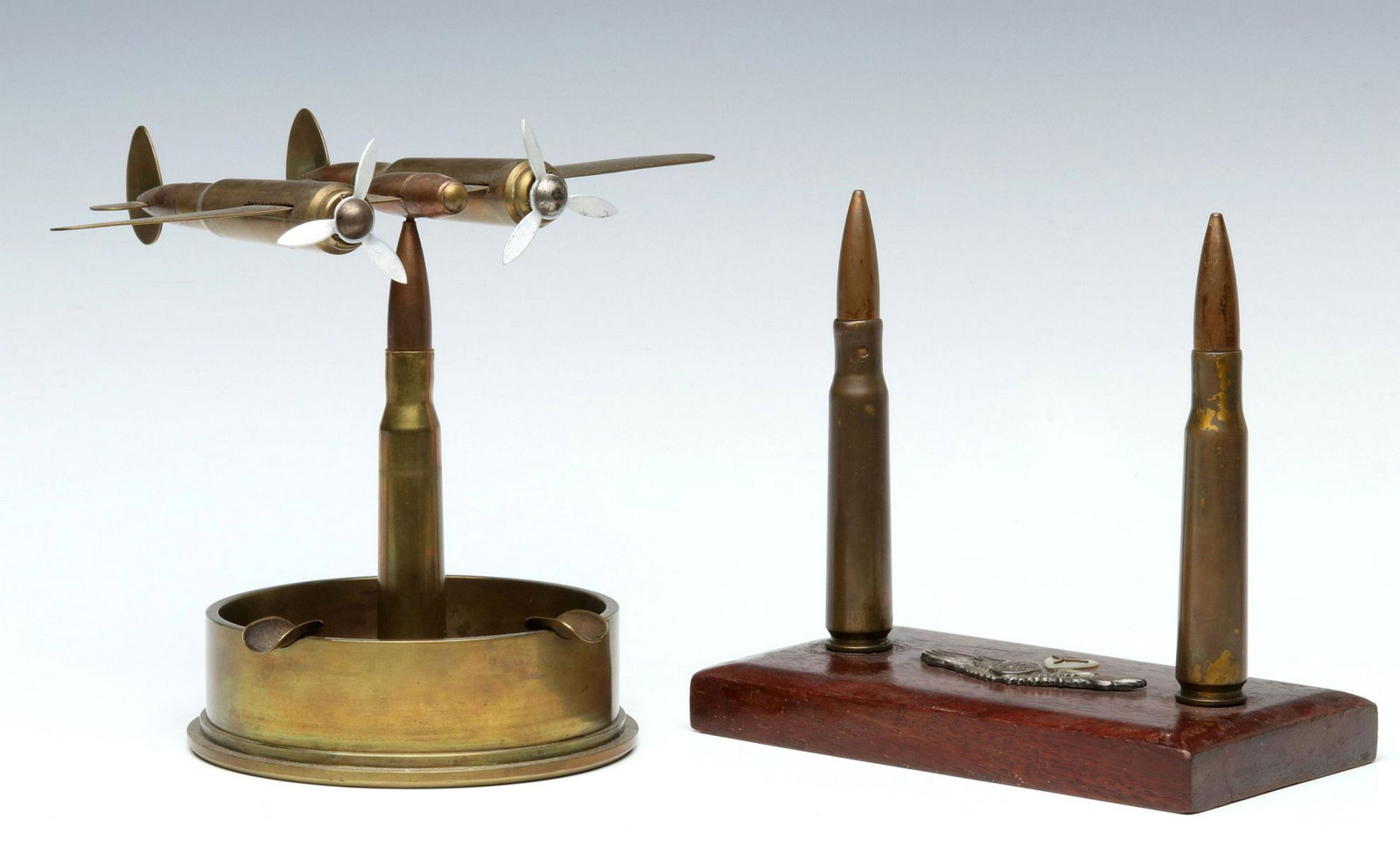 TWO VINTAGE TRENCH ART SCULPTURES: Depiction of an airplane from cartridges and an artillery shell base offered with a desk plaque displaying insignia and two large cartridges. Plan measures 7 x 8.5, stand measures 6.25 x 7 inches. Pro