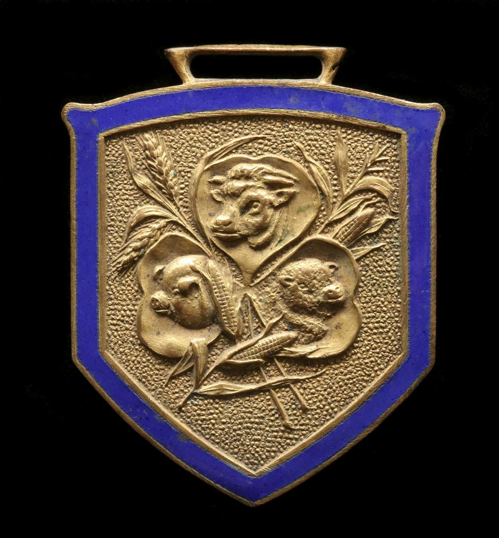 A WOODSON FENNEWALD LIVESTOCK COMMISSION ENAMELED FOB: The gold-tone fob with embossed design of livestock within blue enamel border, lettering back side. Measures 1.75 inches. Provenance: The 45-year collection of Michael and Donna Hayes, West Plains, Mi