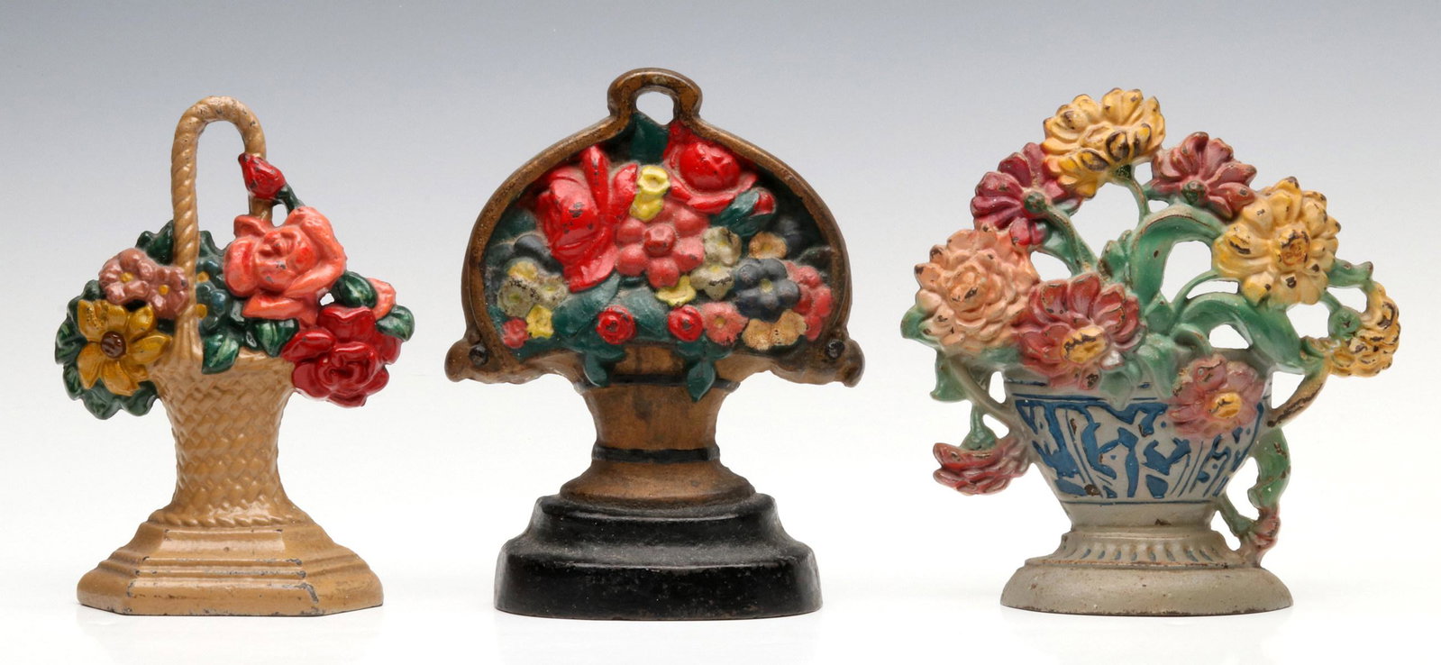 THREE VINTAGE FLOWER BASKET DOOR STOPS: The Hubley 'Zinnias' #267 and 'Flower Basket' #152, single sided, polychrome finish doorstops; plus an A.M. Greenblatt flower basket #79, single sided, polychrome finish. Measure 7.25 to 7.5 inches. P