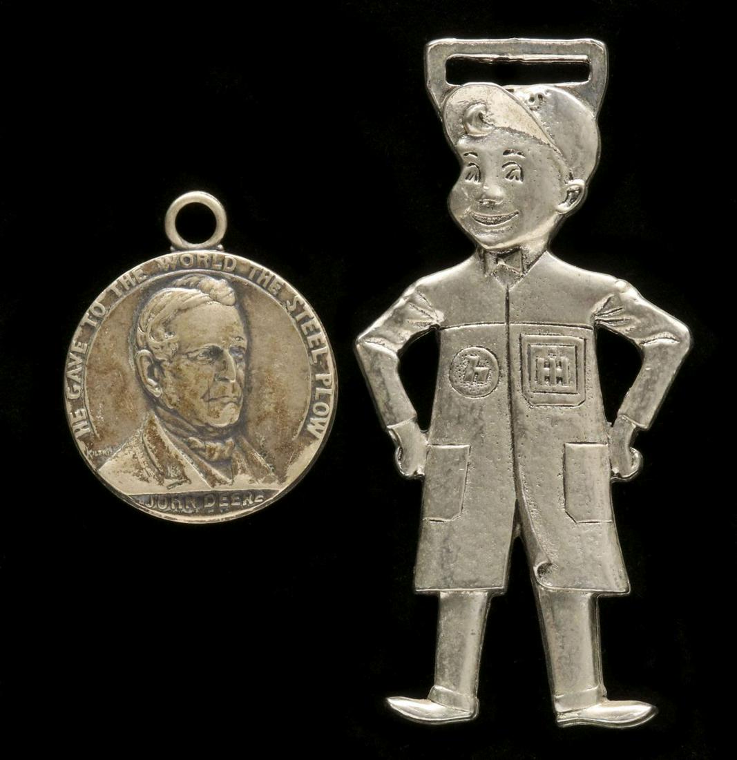 AN UNUSUAL INTERNATIONAL HARVESTER FOB, PLUS JOHN DEERE: Two silver tone fobs as shown. Measure 1.25 and 2.625 inches. Provenance: The 45-year collection of Michael and Donna Hayes, West Plains, Missouri. We happily provide seamless in-house packing and shi