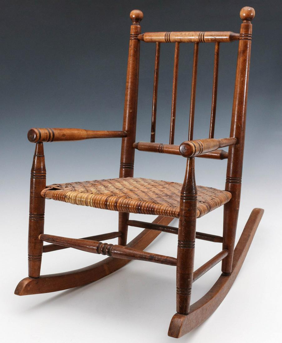 A CIRCA 1900 CHILD'S ROCKING CHAIR WITH RATTAN SEAT: The rocking chair with spindle back, turned arms and framework, woven rattan seat. Measures 21.5 x 14 x 22.5 inches. We happily provide seamless in-house packing and shipping services on nearly everyt