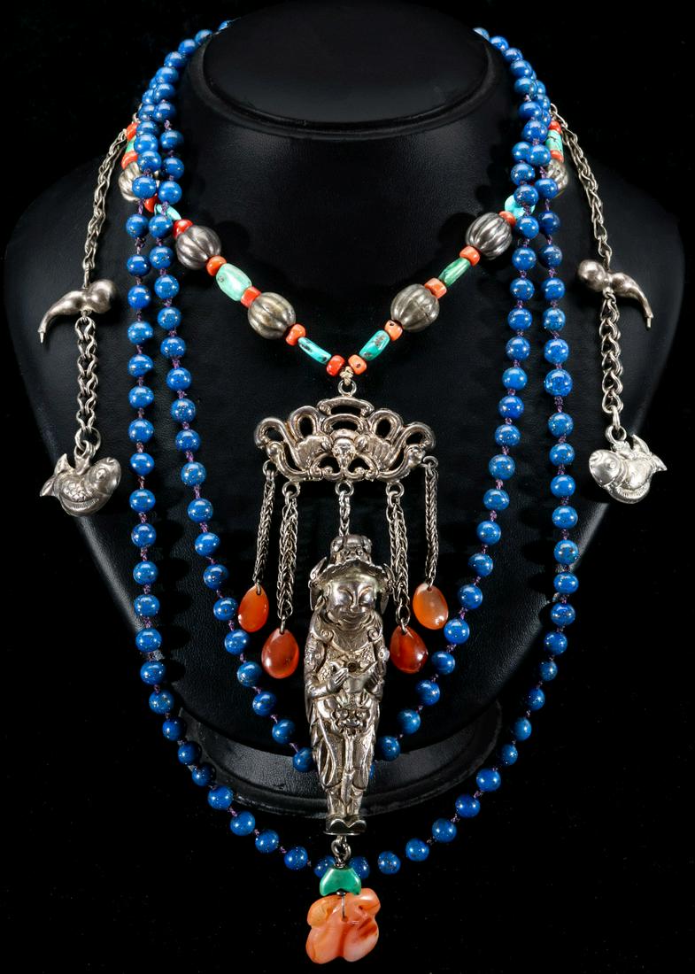 A CHINESE NECKLACE OF SILVER AND SEMI-PRECIOUS STONES: Two necklaces: an elaborate Chinese necklace with a three-dimensional full length figure with carnelian drop and suspended from an ornament with four smaller carnelian pendants, the whole suspended fr