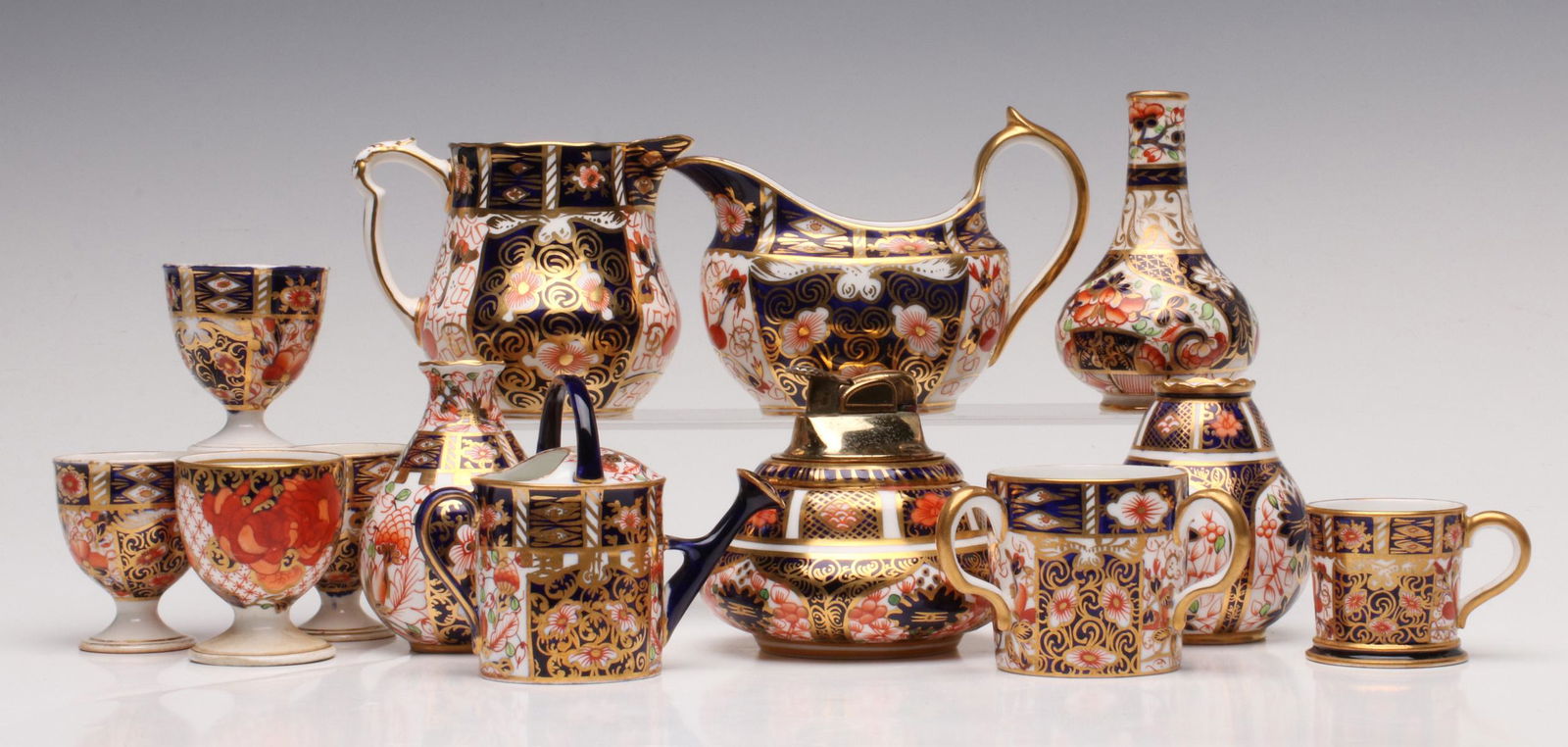 A MIXED LOT OF SMALL ROYAL CROWN DERBY CABINET PIECES: The group includes an early bottle vase with hand painted red crown mark, small egg cups in similar decoration but unmarked, creamers, watering can, table lighter base, cups and more. Measures 1.5 to