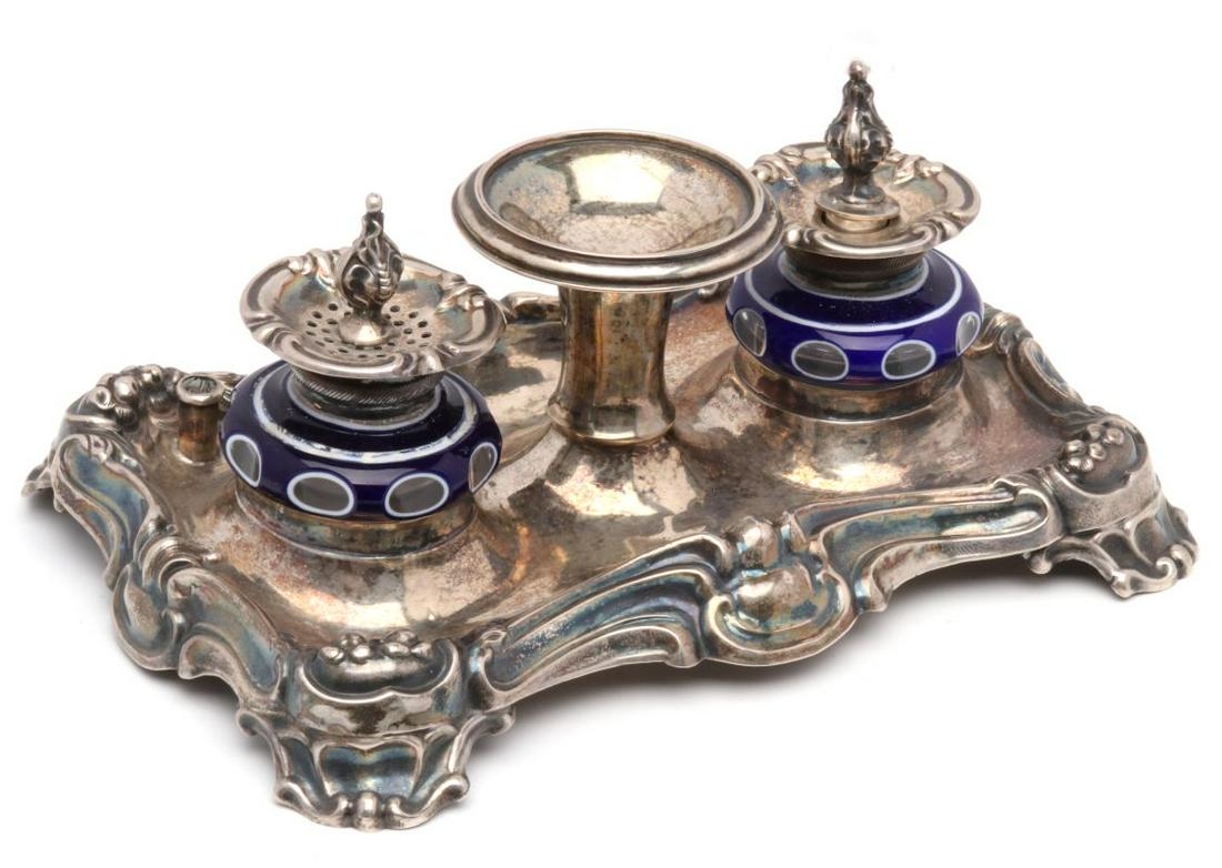 A FINE SILVER AND OVERLAID GLASS CUT-TO-CLEAR INKWELL: The .800 silver double inkstand with triple overlaid glass well and sander cut-to-clear, two pen stands and a central trumpet form pedestal served an additional though unidentified purpose, .800 silve