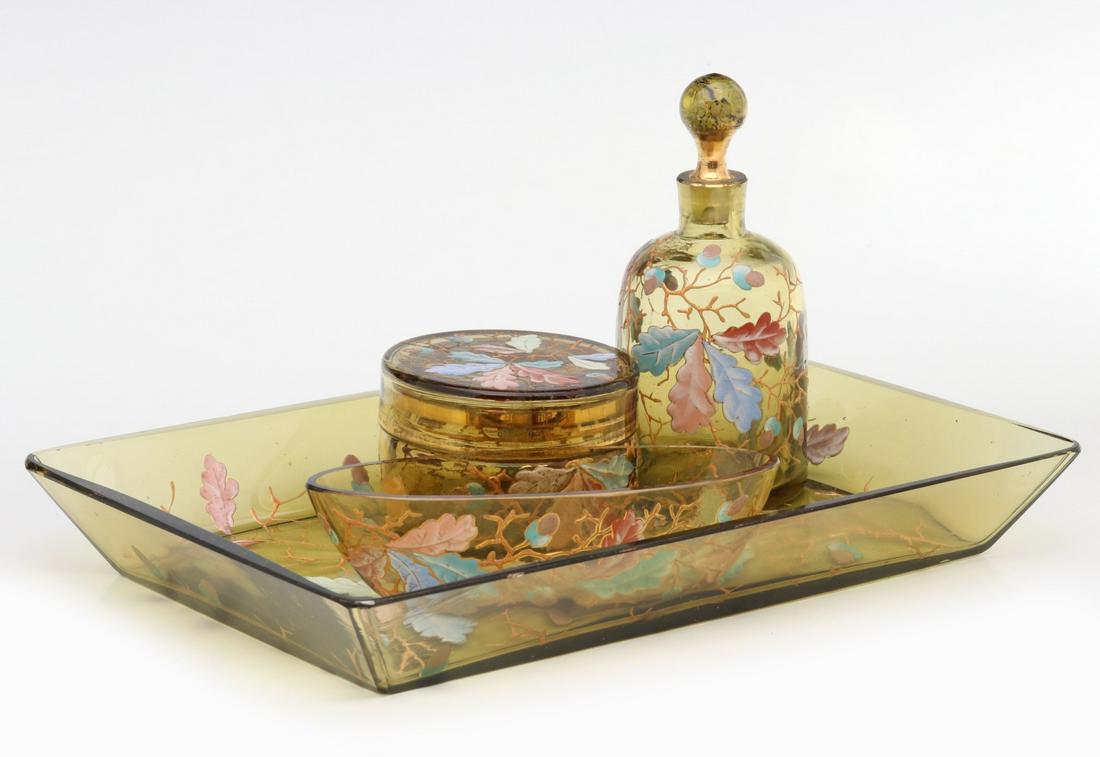 A FOUR PIECE BOHEMIAN ART GLASS DRESSER SET: The amber glass dresser set decorated enameled in oak leaves and acorns, includes an oval trinket bowl, perfume, powder jar and tray, spurious etched Moser signatures throughout. Measures 1.5 x 9.5 x 