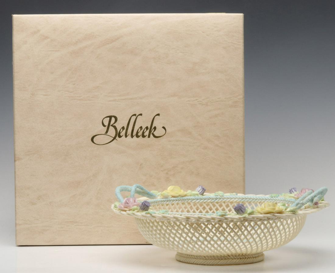 AN IRISH BELLEEK PORCELAIN BASKET IN THE ORIGINAL BOX: The two-handled basket with applied porcelain flowers and clover centered by a four strand woven base, the pearl and polychrome glaze on basketry and flowers, signed under the base with porcelain tags
